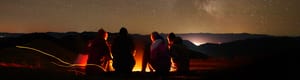 A group of campers around a campfire under a sky filled with stars. 